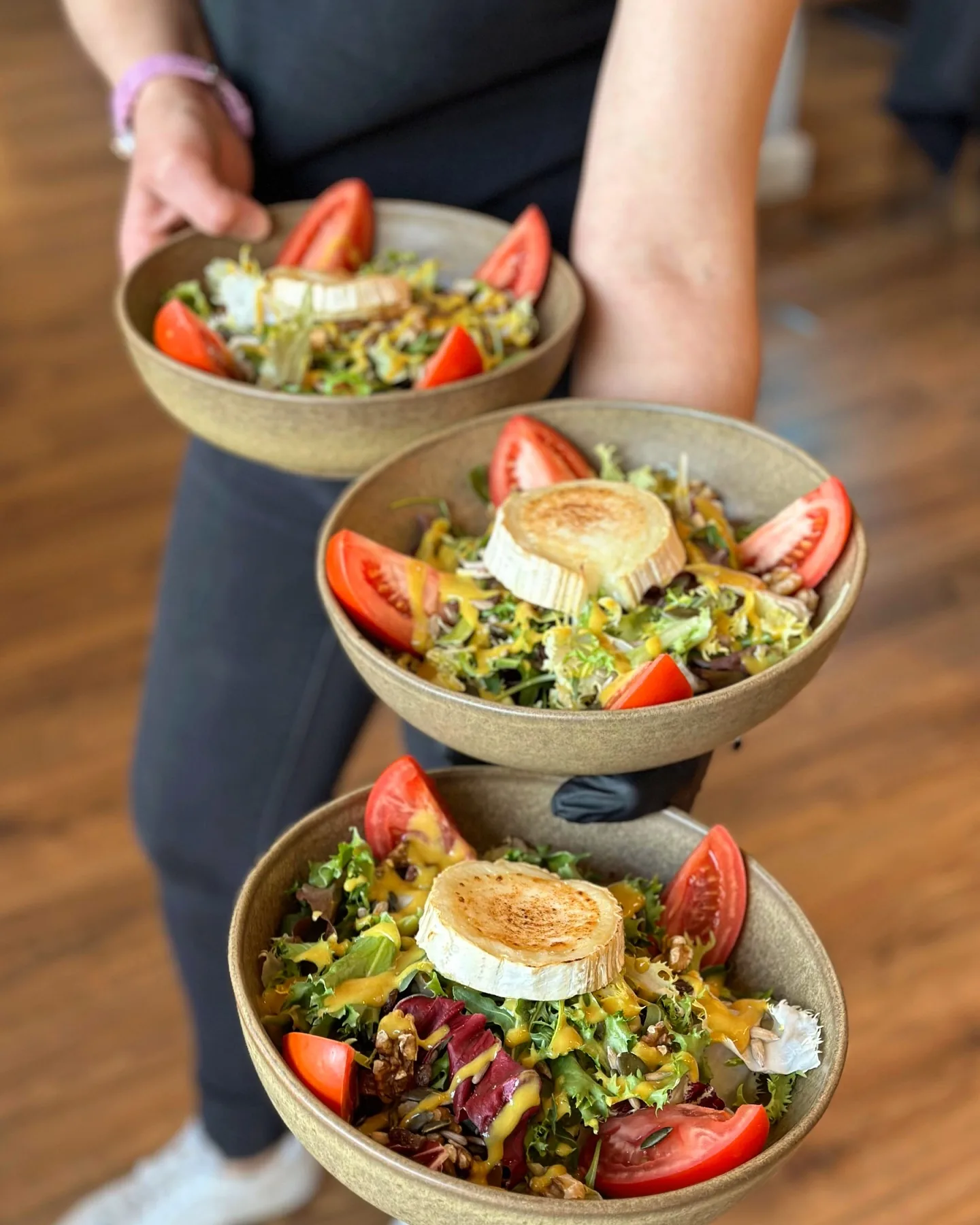 Three salads with grilled goat cheese on their way to the table